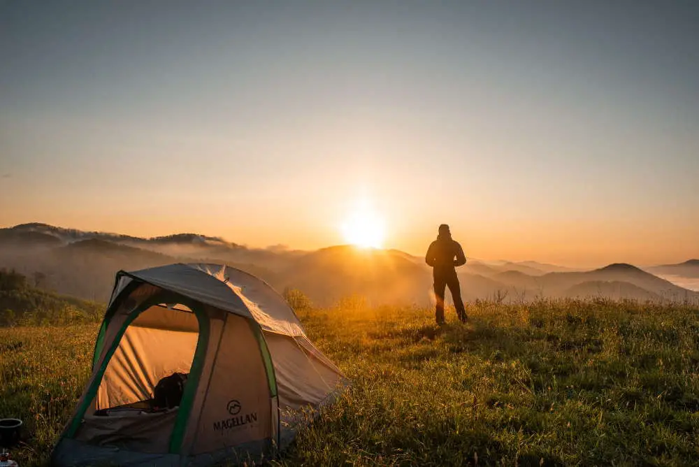 man looking at sun with tent behind him